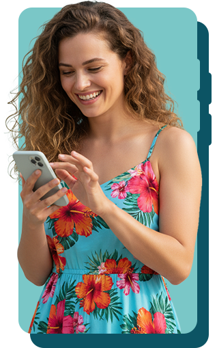 A smiling woman with long curly hair wearing a blue floral dress, holding and looking at a light-colored smartphone against a teal background.